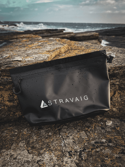 Black Stravaig Trinkie Zip Bag on a rocky surface near the ocean