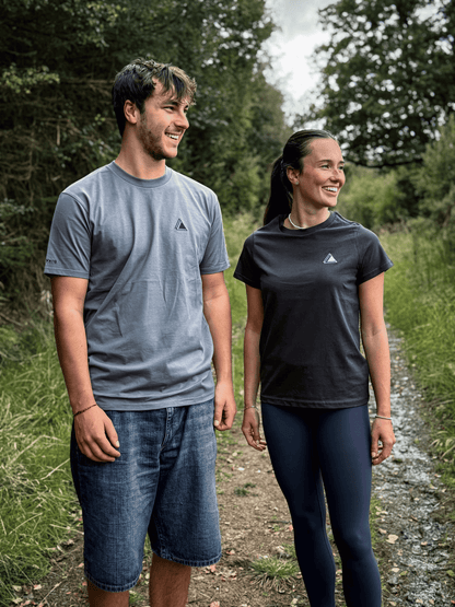 Man in the Haar Grey mens t-shirt and woman in the Sgàil Grey womens t-shirt walking a forest trail