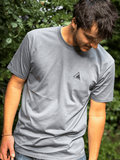 Man looking down in the Stravaig Mens Everyday Trail T-Shirt in Haar Grey against green leaves