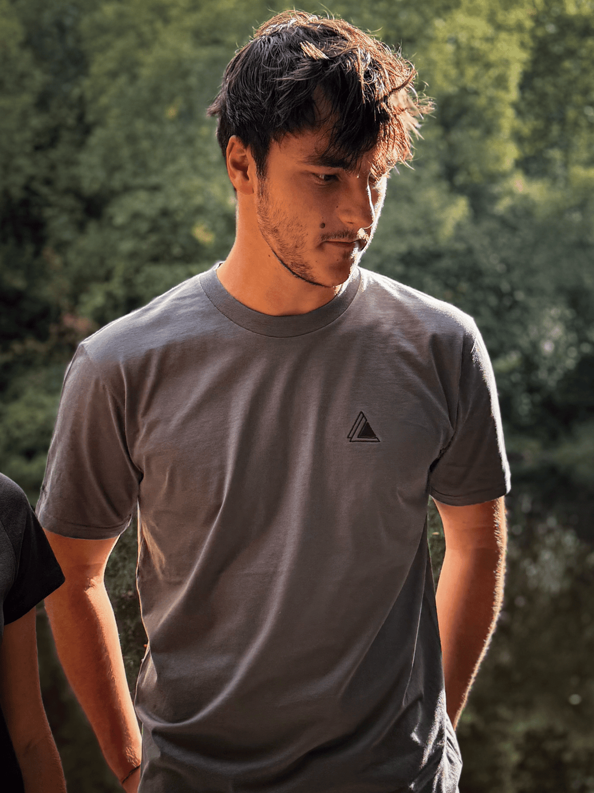 Man in a Haar Grey Stravaig t-shirt standing in dappled woodland light