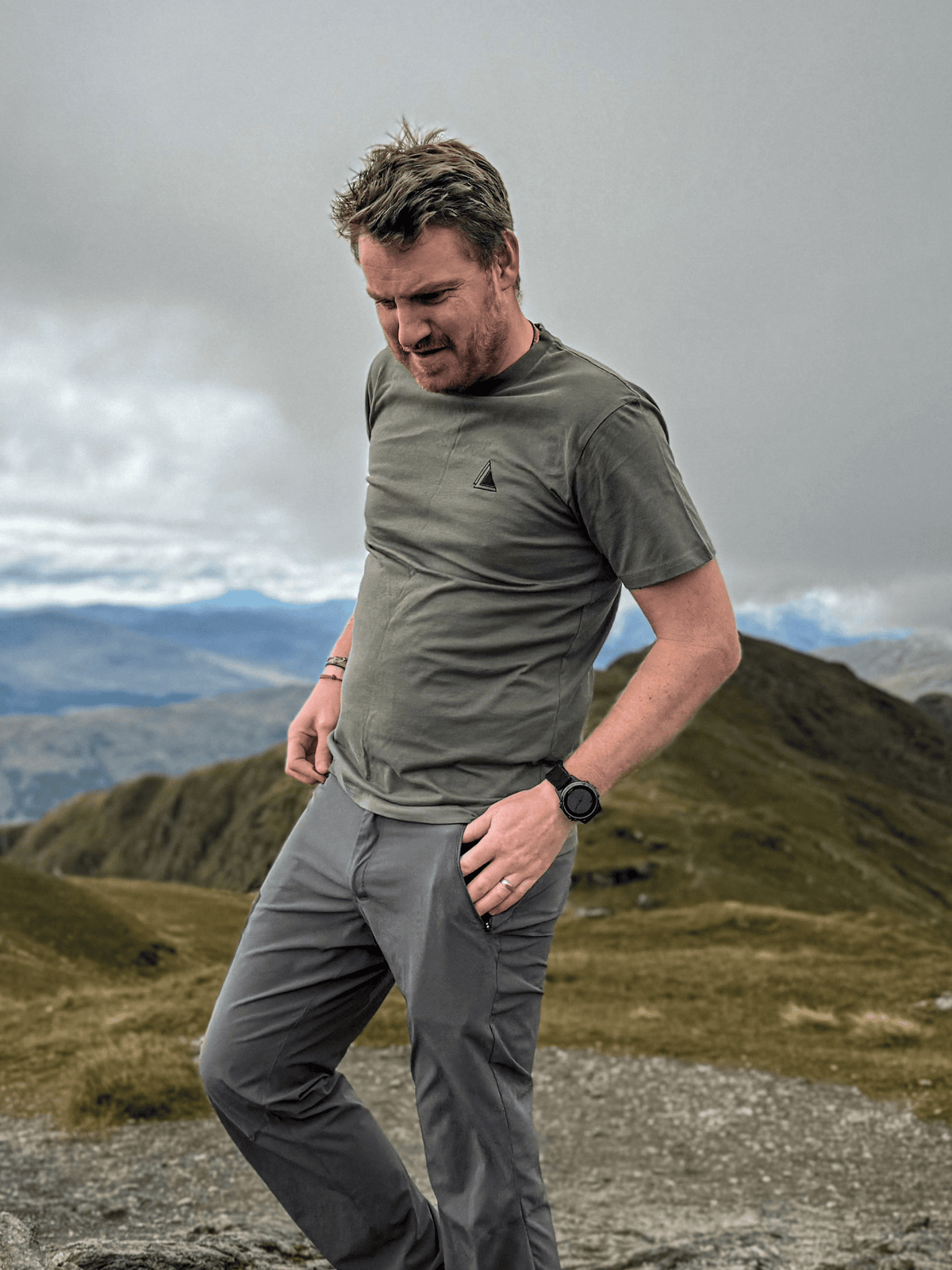 Man wearing the Stravaig Mens Everyday Trail T-Shirt in Highland Moss on a Scottish mountain summit