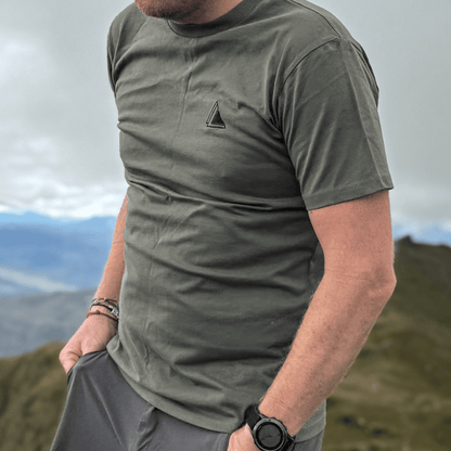 Man in the Highland Moss Stravaig t-shirt on a hilltop with mountain views behind