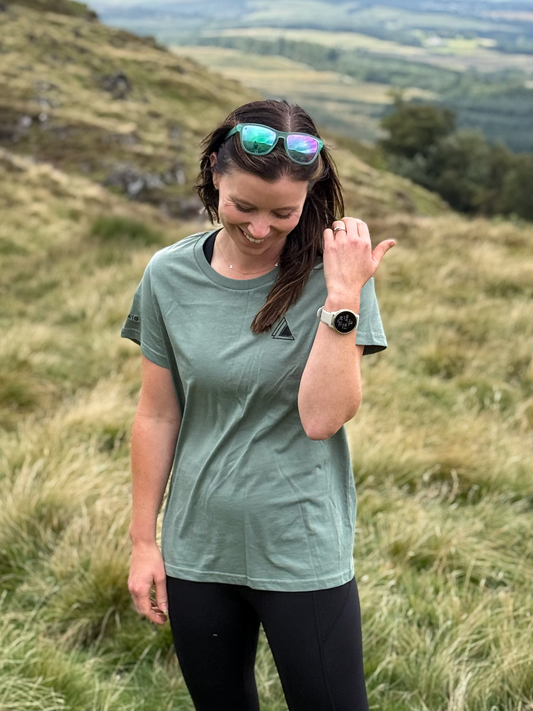 Woman wearing the Stravaig Womens Everyday Trail T-Shirt in Machair Sage on a grassy Scottish hillside