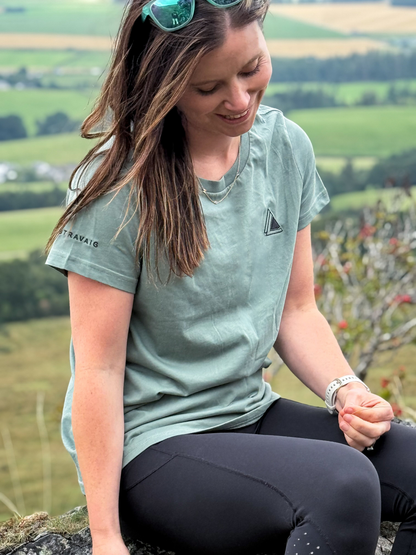 Woman in a Machair Sage Stravaig t-shirt sitting on a hilltop overlooking green fields