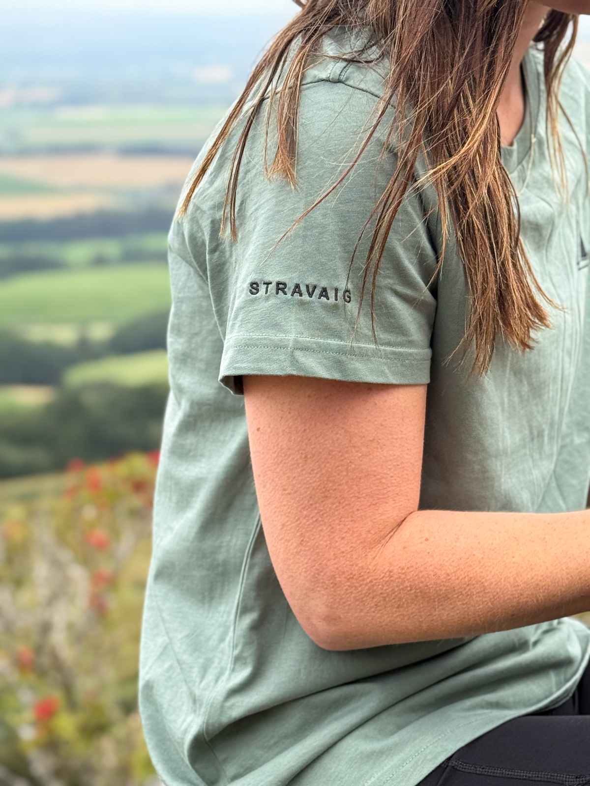 Close-up of the Stravaig sleeve print on the Machair Sage womens t-shirt with countryside views behind