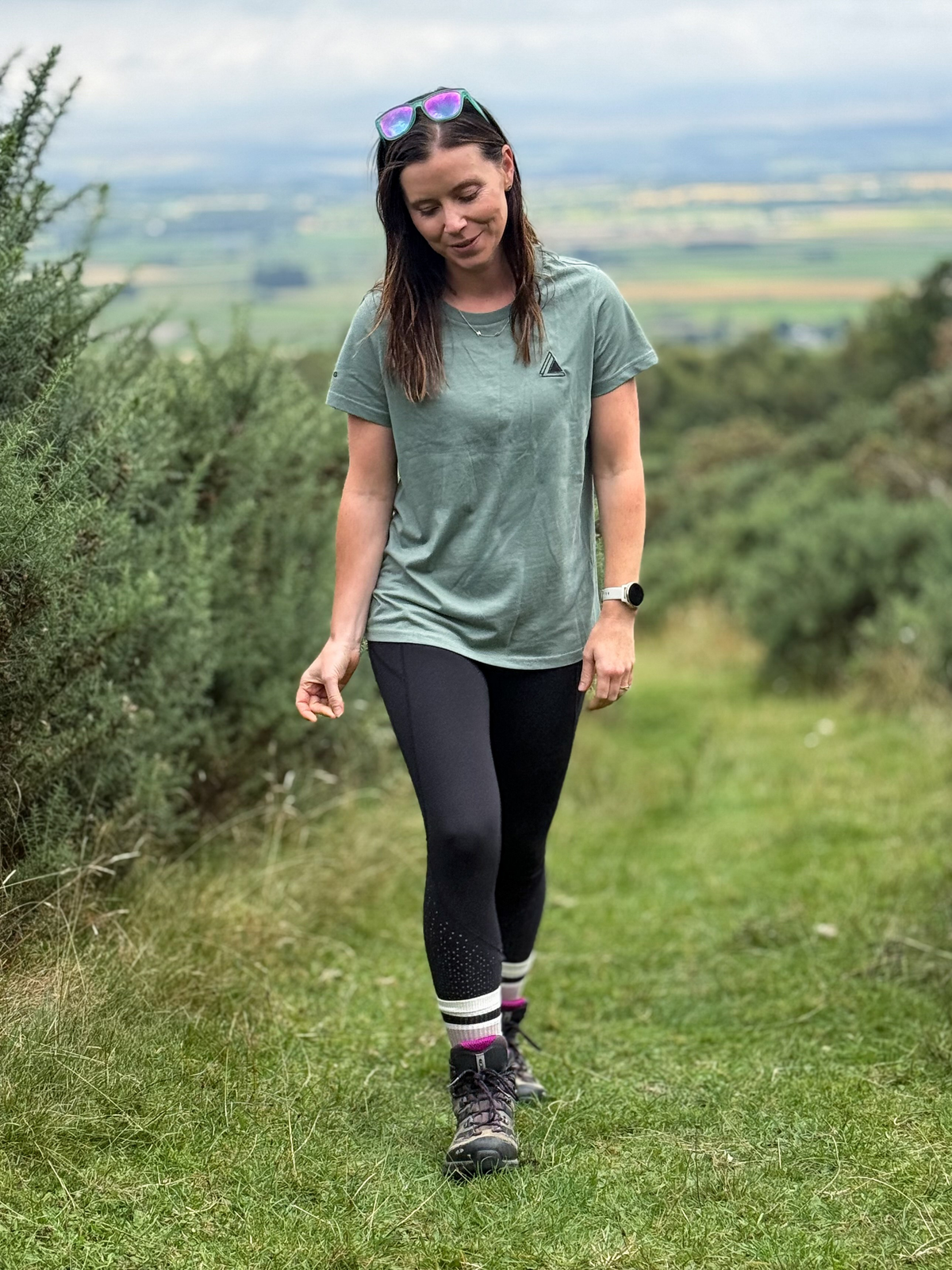 Woman walking down a grassy hill path wearing the Stravaig Womens Everyday Trail T-Shirt in Machair Sage