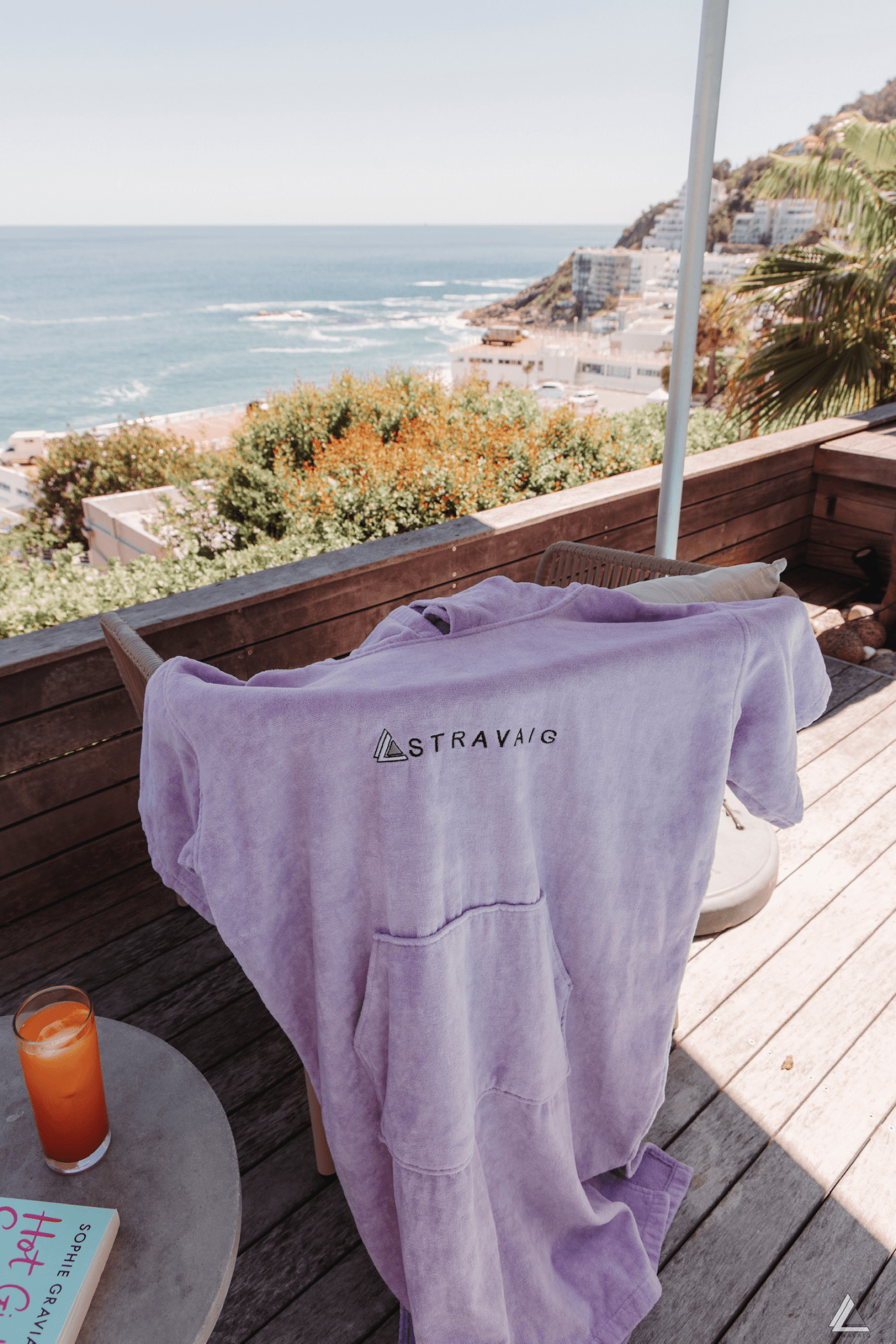 Lilac adult hooded towel with 'Stravaig' logo on a wooden deck with ocean view