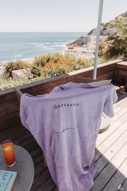 Lilac adult hooded towel with 'Stravaig' logo on a wooden deck with ocean view