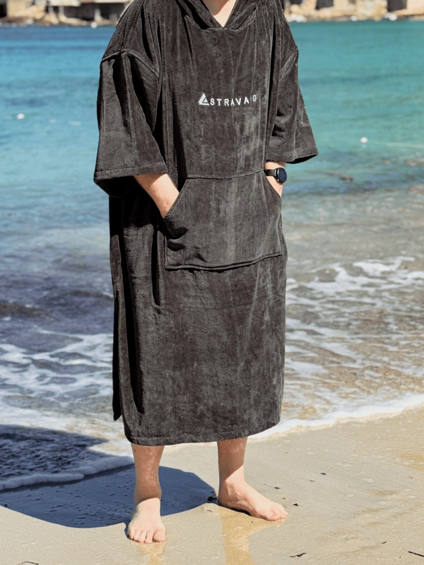 Man wearing a Sgàil Grey beach towel robe on a beach with ocean in the background