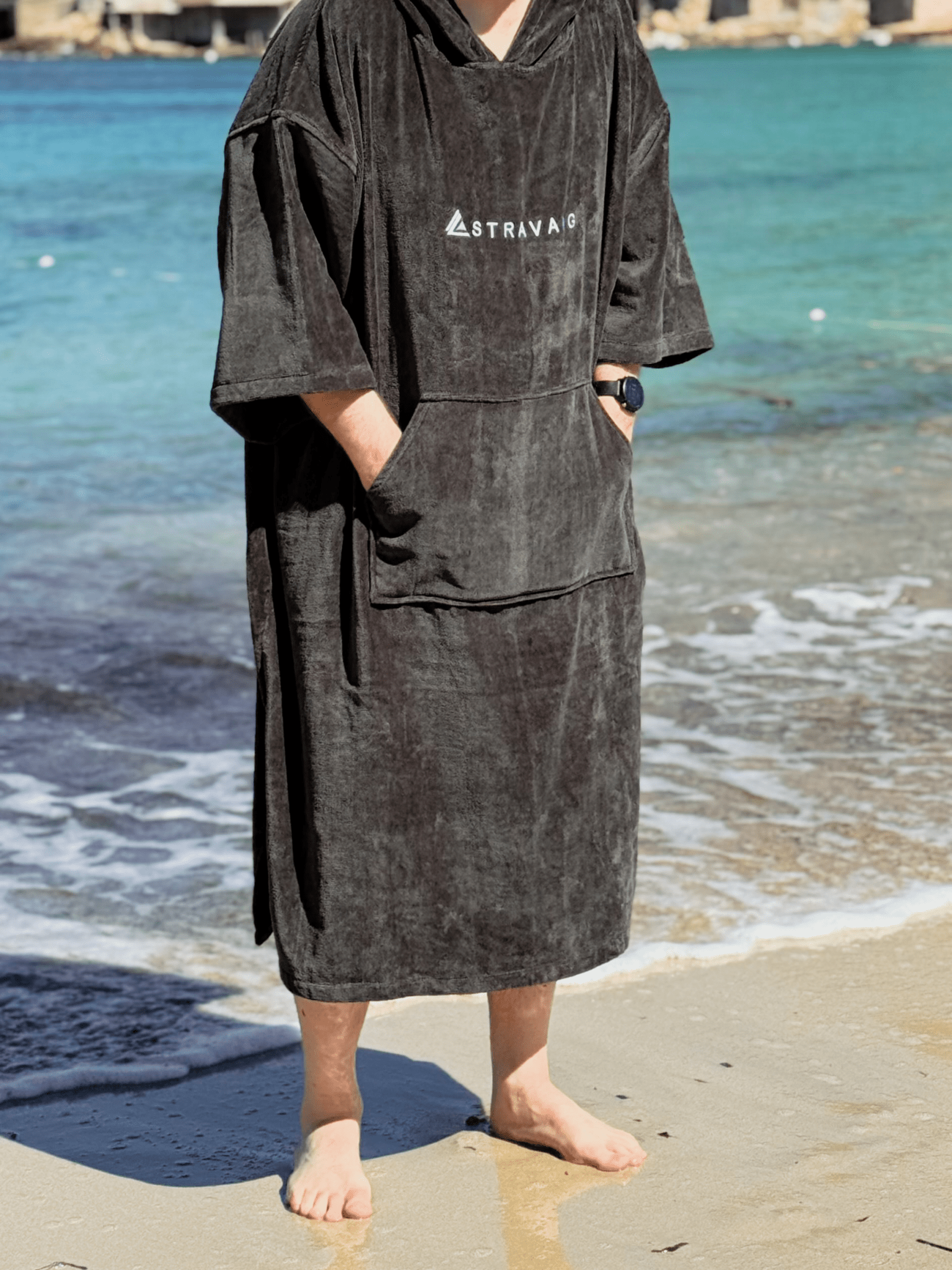Man wearing a Sgàil Grey beach towel robe on a beach with ocean in the background