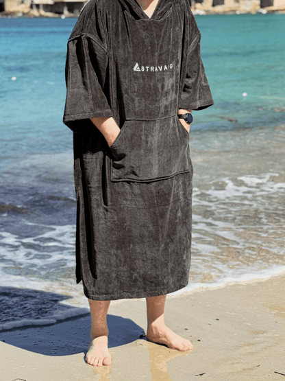 Man wearing a Sgàil Grey beach towel robe on a beach with ocean in the background