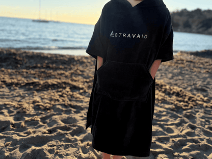 Child wearing a Sgàil Grey 'Stravaig' kids towel robe on a beach with ocean in the background