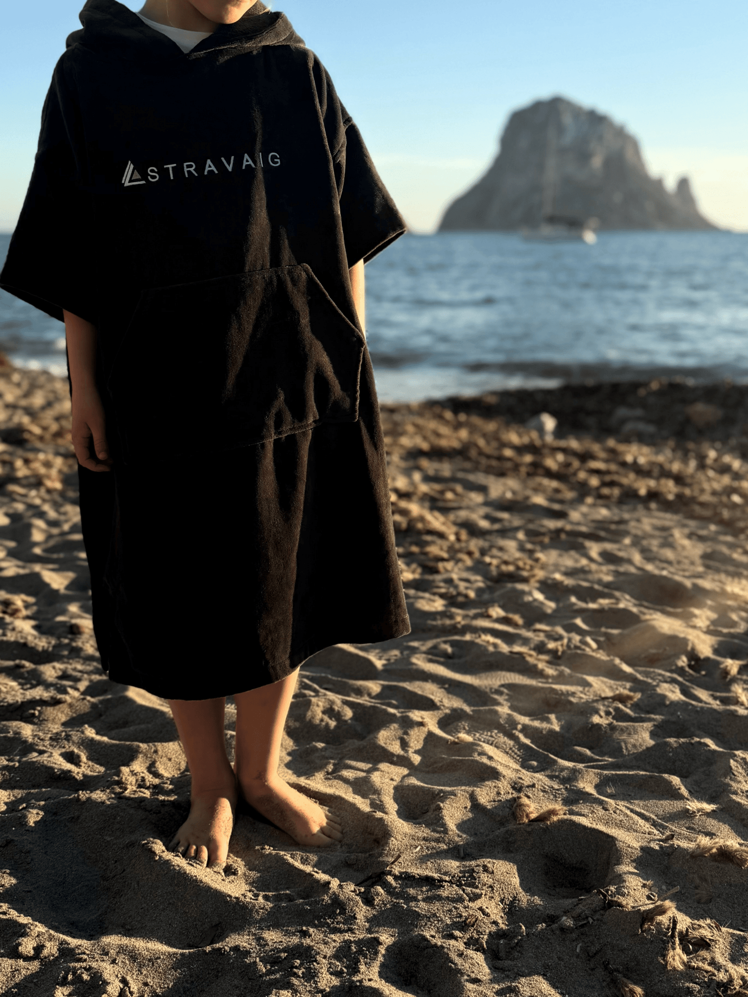 Child wearing a Sgàil Grey Stravaig kids changing towel on a beach with a mountain in the background
