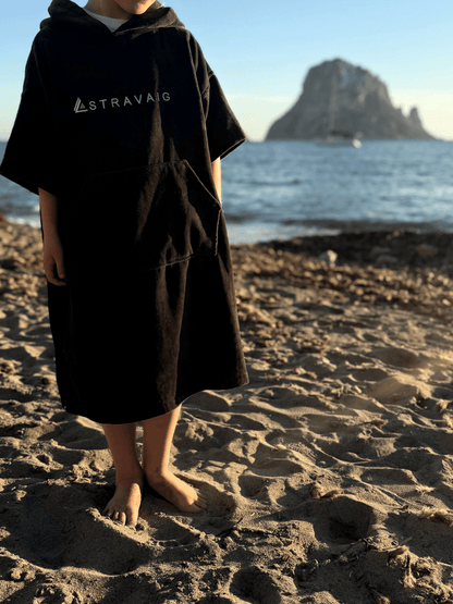 Child wearing a Sgàil Grey Stravaig kids changing towel on a beach with a mountain in the background