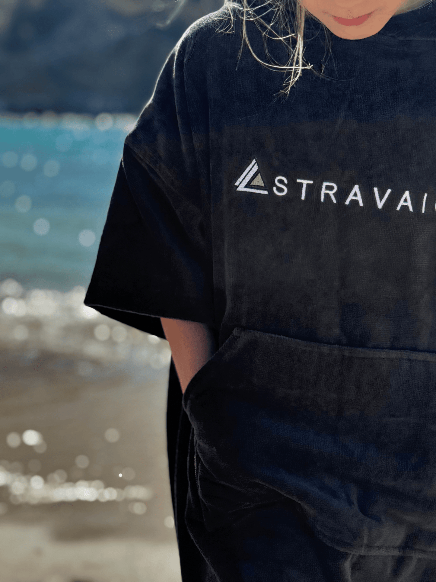Child wearing a Stravaig Sgàil Grey kids changing towel by a body of water.