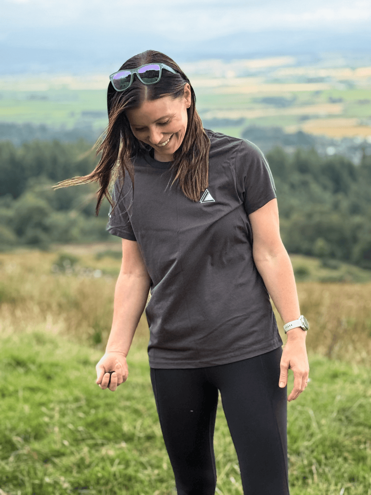 Woman smiling on a grassy hillside wearing the Sgàil Grey Stravaig Everyday Trail T-Shirt