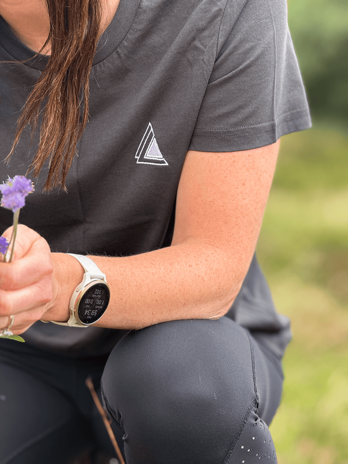Close-up of the Stravaig chest logo on the Sgàil Grey womens t-shirt as she picks a wildflower