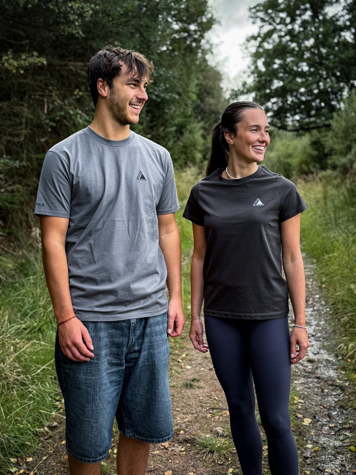 Man in the Haar Grey mens t-shirt and woman in the Sgàil Grey womens t-shirt walking a forest trail